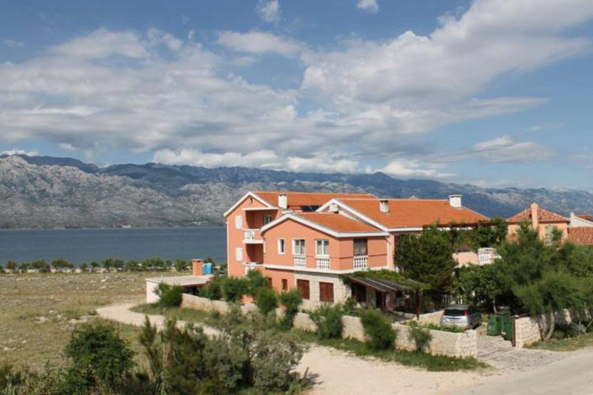 A two-story building with a red roof, surrounded by greenery and a view of mountains in the background.