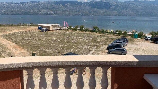 A view of a beach with a parking area, a small building, and mountains in the background. - Apartments Ata (Razanac)