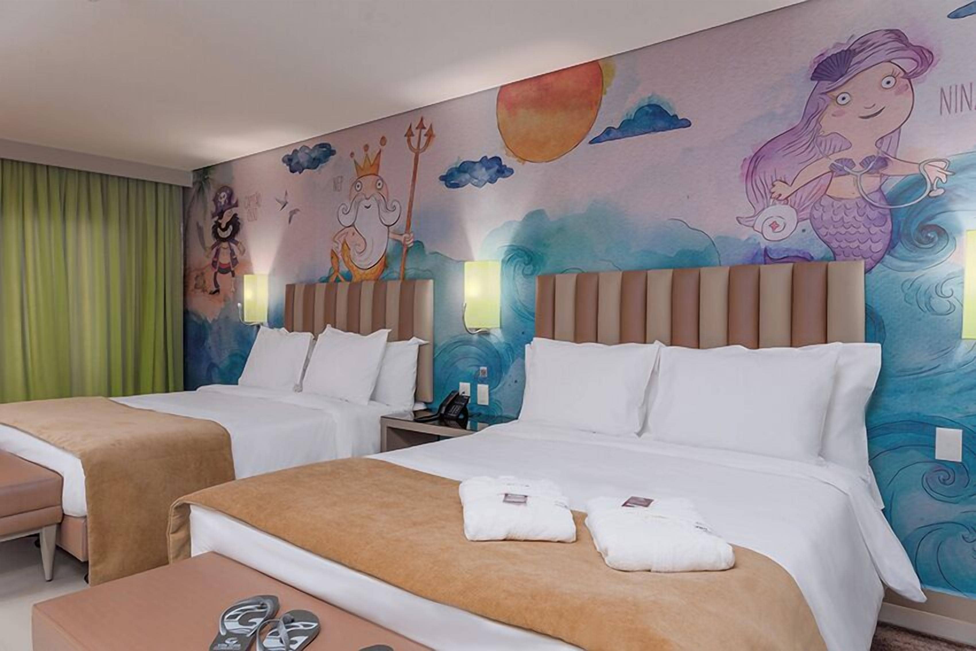 Habitación de hotel con dos camas, un escritorio y un mural en la pared.