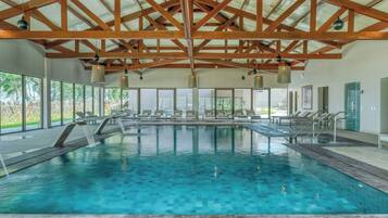 Une piscine intérieure à l’eau claire, avec des poutres en bois et des chaises longues.