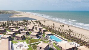 A resort with multiple bungalow-style buildings, a central swimming pool, and a beach with palm trees. - Vila Galé Collection Sunset Cumbuco (Caucaia)