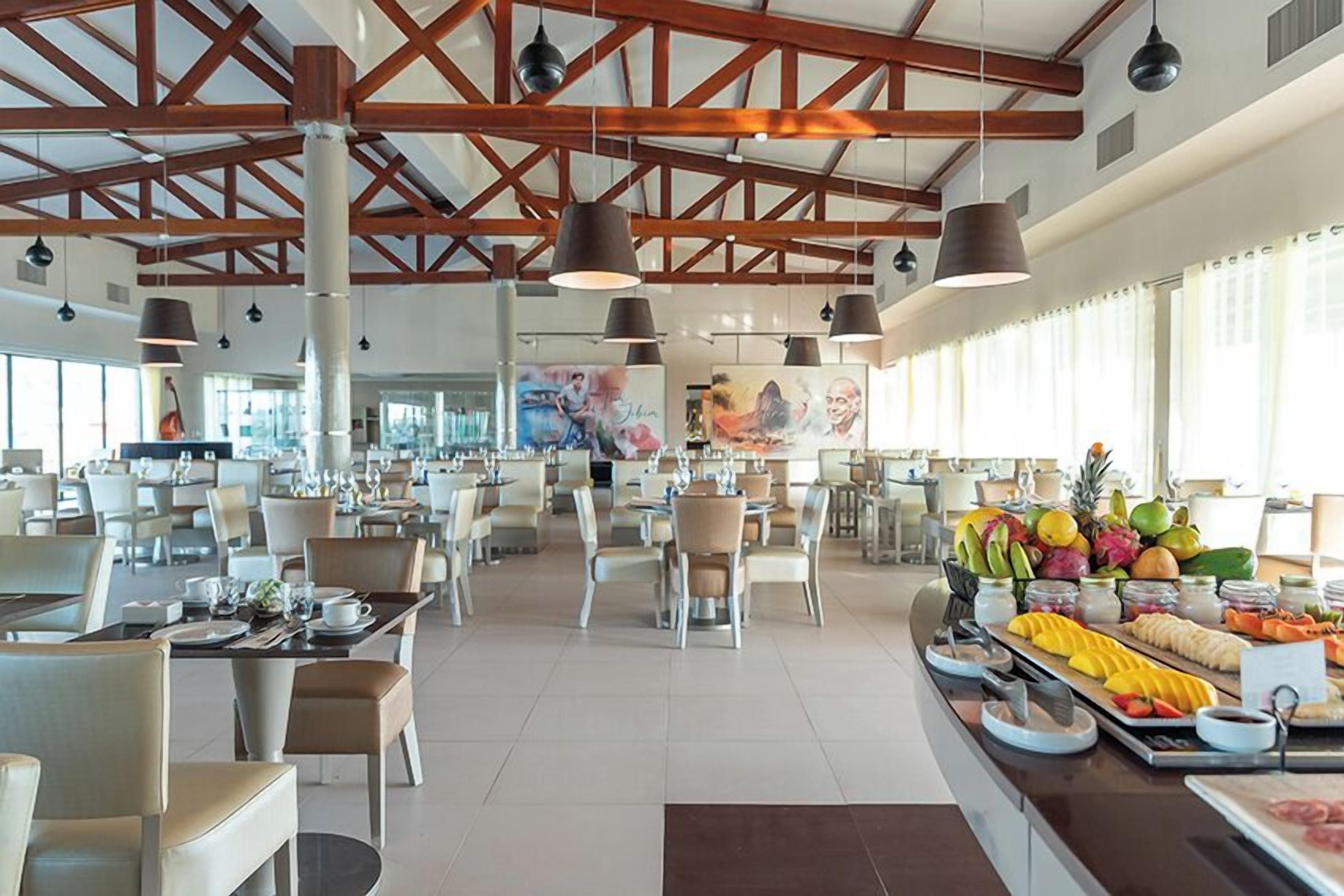 A spacious dining area with high ceilings, exposed beams, and pendant lighting. Tables are set with white tablecloths and various dishes.