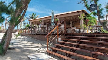 Una propiedad frente a la playa con una escalera que lleva a un área de estar cubierta al aire libre, palmeras y un cartel que dice