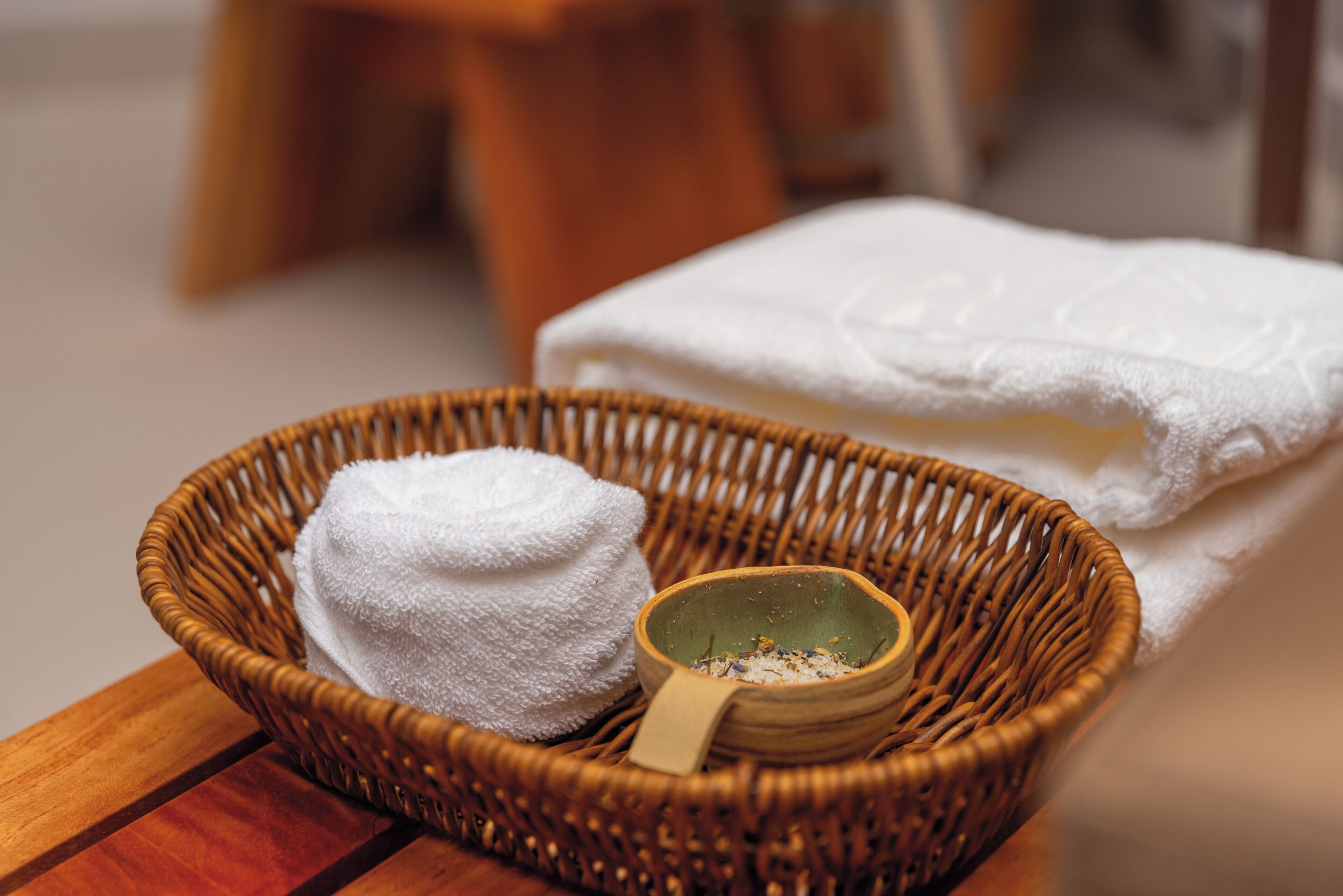 Una cesta de mimbre con una toalla blanca y un cuenco pequeño con asa de madera.
