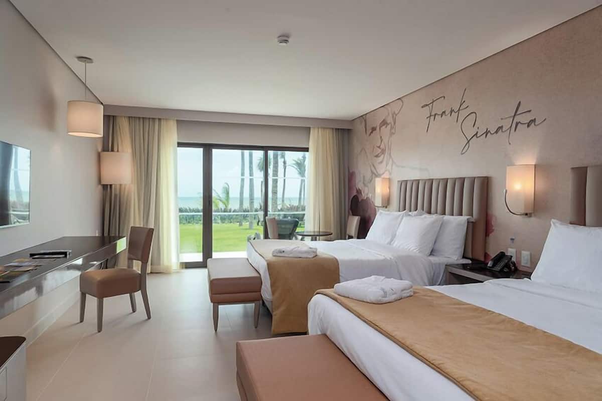 A hotel room with two beds, a desk, a chair, and a view of the outdoors.