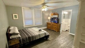 A bedroom with a bed, dresser, TV, and a bathroom visible through an open door. - Roomy Beachfront Apartment, Deck, Game Room! 2 Bedroom Apts by RedAwning (Norfolk)