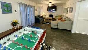 A living room with a foosball table, a sofa, a television, and a window with curtains. - Roomy Beachfront Apartment, Deck, Game Room! 2 Bedroom Apts by RedAwning (Norfolk)