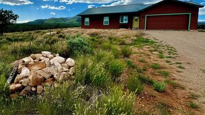 A red house with a green door and windows, surrounded by a gravel driveway and grassy area. - Yellow Door Retreat I Mountain Views I Privacy I 30 Minutes to Moab! (La Sal)