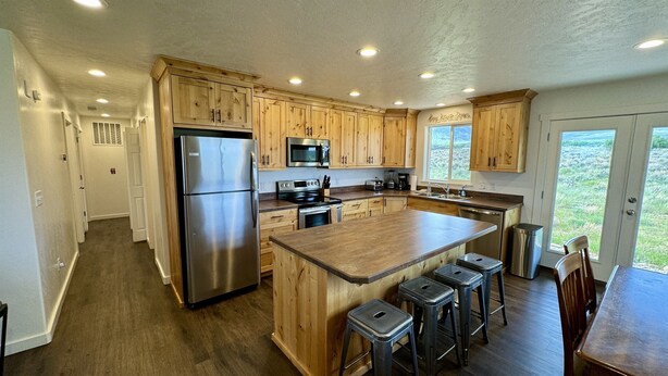 A modern kitchen with wooden cabinets, stainless steel appliances, and a large island with bar stools. - Yellow Door Retreat I Mountain Views I Privacy I 30 Minutes to Moab! (La Sal)