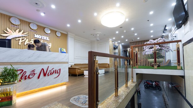 A hotel reception area with a wooden reception desk, a clock, and a sign that reads "Pho Nang."