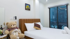 A bedroom with a bed, a ceiling fan, a bedside table with a teddy bear, a window, and a door.