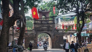 A street with a prominent archway, lined with trees and flags, and various shops and parked motorcycles.