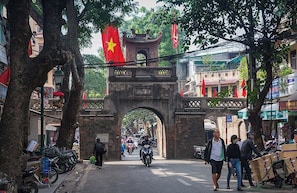 A street with a prominent archway, lined with trees and flags, and various shops and parked motorcycles.