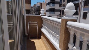 Ein schmaler Balkon mit Fliesenboden, weißer Brüstung und einer Metallleiter.