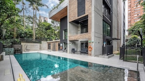 A modern building with a swimming pool, outdoor seating, and a gated entrance.