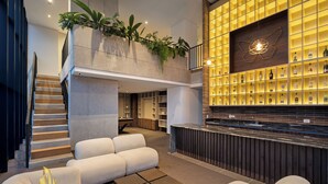 A modern lobby with a staircase, seating area, and a bar with shelves of bottles.