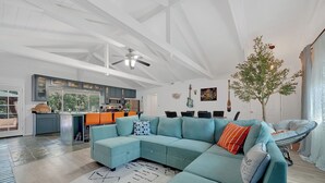 A spacious living area with a teal sectional sofa, a large rug, and a ceiling fan.