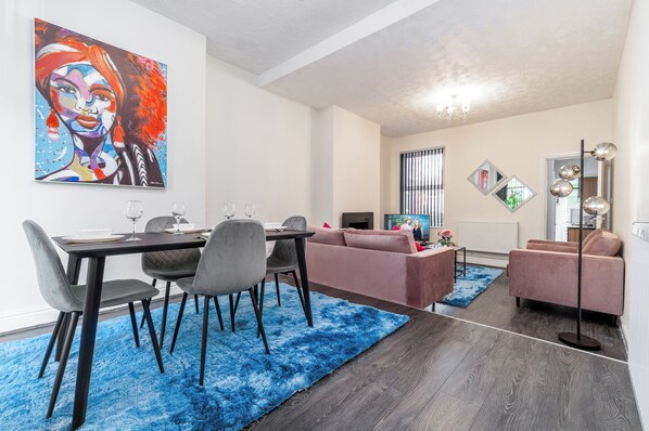 A modern living room with a dining area, featuring a blue shag rug, a pink sofa, and a large abstract painting on the wall. - Spacious 2 bed House With Free on Street Parking (Birmingham)
