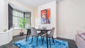 A dining area with a table, chairs, a blue rug, a potted plant, and a painting on the wall. - Spacious 2 bed House With Free on Street Parking (Birmingham)