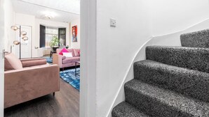 A modern living room with a pink sofa, a staircase with grey carpet, and a white wall. - Spacious 2 bed House With Free on Street Parking (Birmingham)