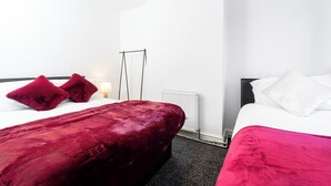 A hotel room with two beds, one with red and white bedding and the other with white bedding. There is a radiator on the wall and a lamp on the side table. - Spacious 2 bed House With Free on Street Parking (Birmingham)