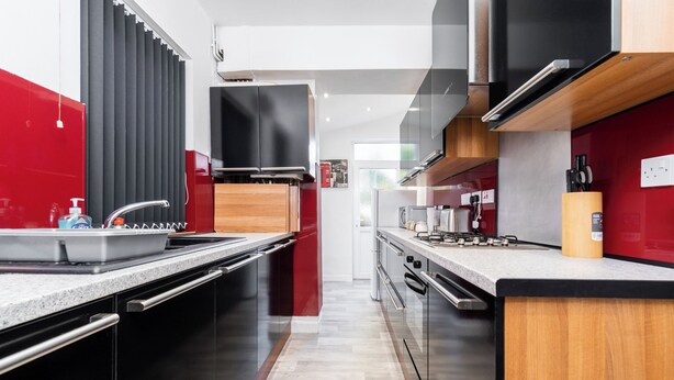 A modern kitchen with a central island, stainless steel appliances, and a red accent wall. - Spacious 2 bed House With Free on Street Parking (Birmingham)