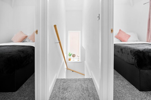 Un pasillo estrecho con una puerta de madera, un ventanal pequeño y dos camas con ropa de cama blanco y negro.