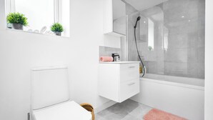 A modern bathroom with a toilet, a shower, a vanity with a mirror, and a small window with plants. - Family/contractors 3 bed House/parking/sleeps 7 (Bilston)