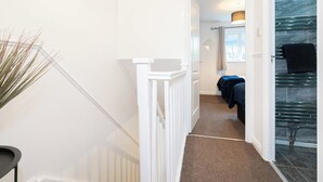 A hallway with a white railing, a plant, and a glimpse of a room with a bed and a glass shower. - 2 Bed-sleeps 4-private Garden- Free Parking (Birmingham)