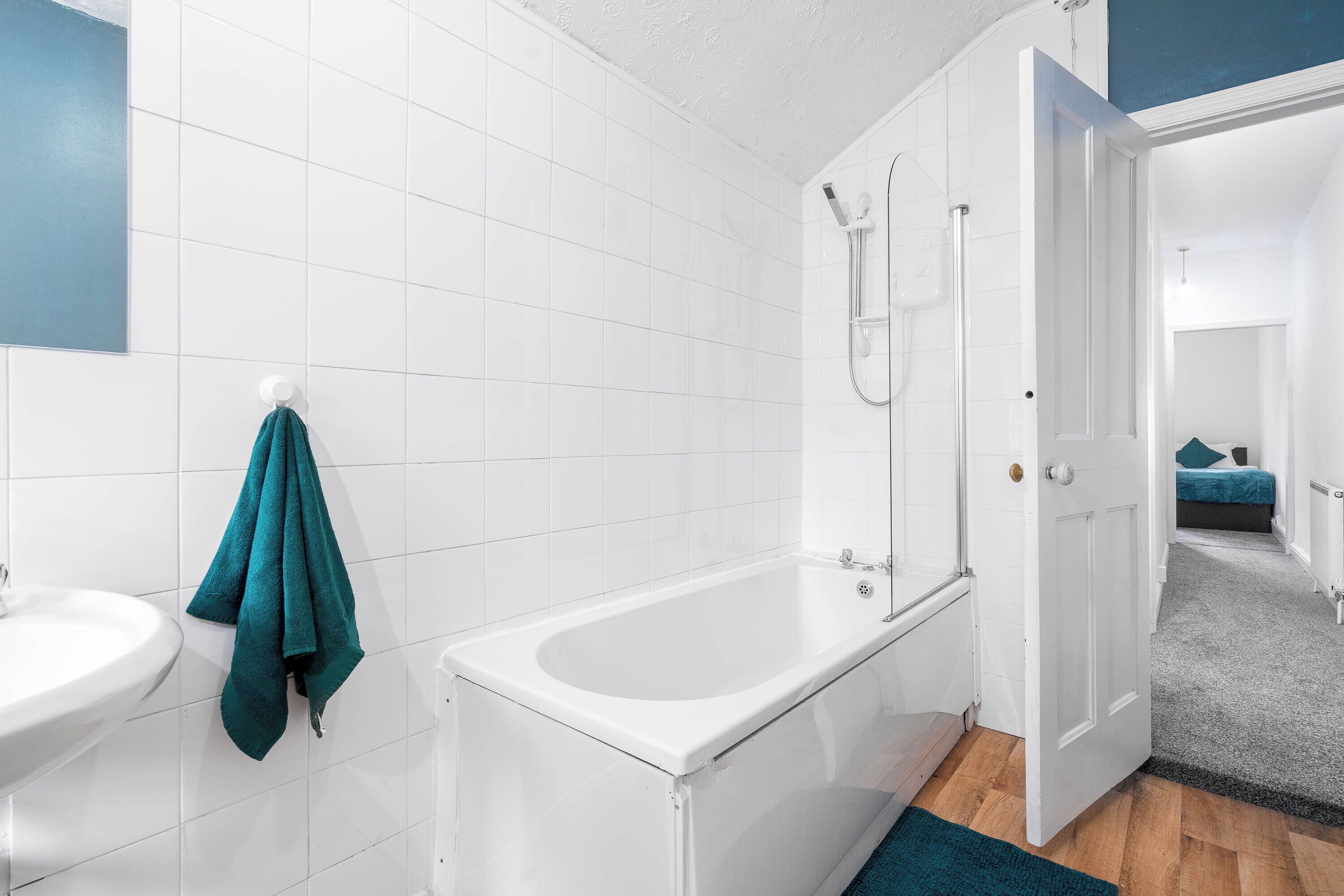 Une salle de bain avec des carreaux blancs, une baignoire, une douche et un lavabo.