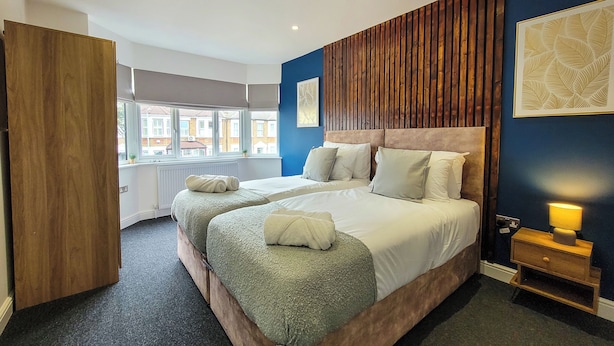 Une chambre d’hôtel avec un grand lit, une armoire en bois, une fenêtre donnant sur des immeubles et une table de chevet avec une lampe.