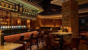 A bar area with a brick wall, wooden bar counter, and seating with tables and chairs. - The James Hotel (Tralee)