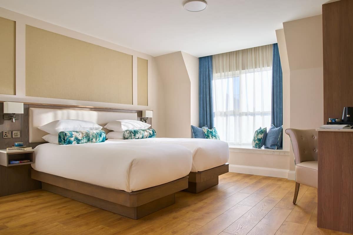 Une chambre d’hôtel avec un grand lit, une table de chevet, un bureau et une fenêtre avec des rideaux.