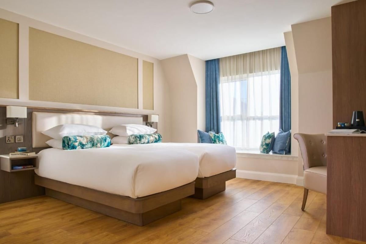 Une chambre d’hôtel avec un grand lit, des tables de chevet, un bureau et une fenêtre avec des rideaux.