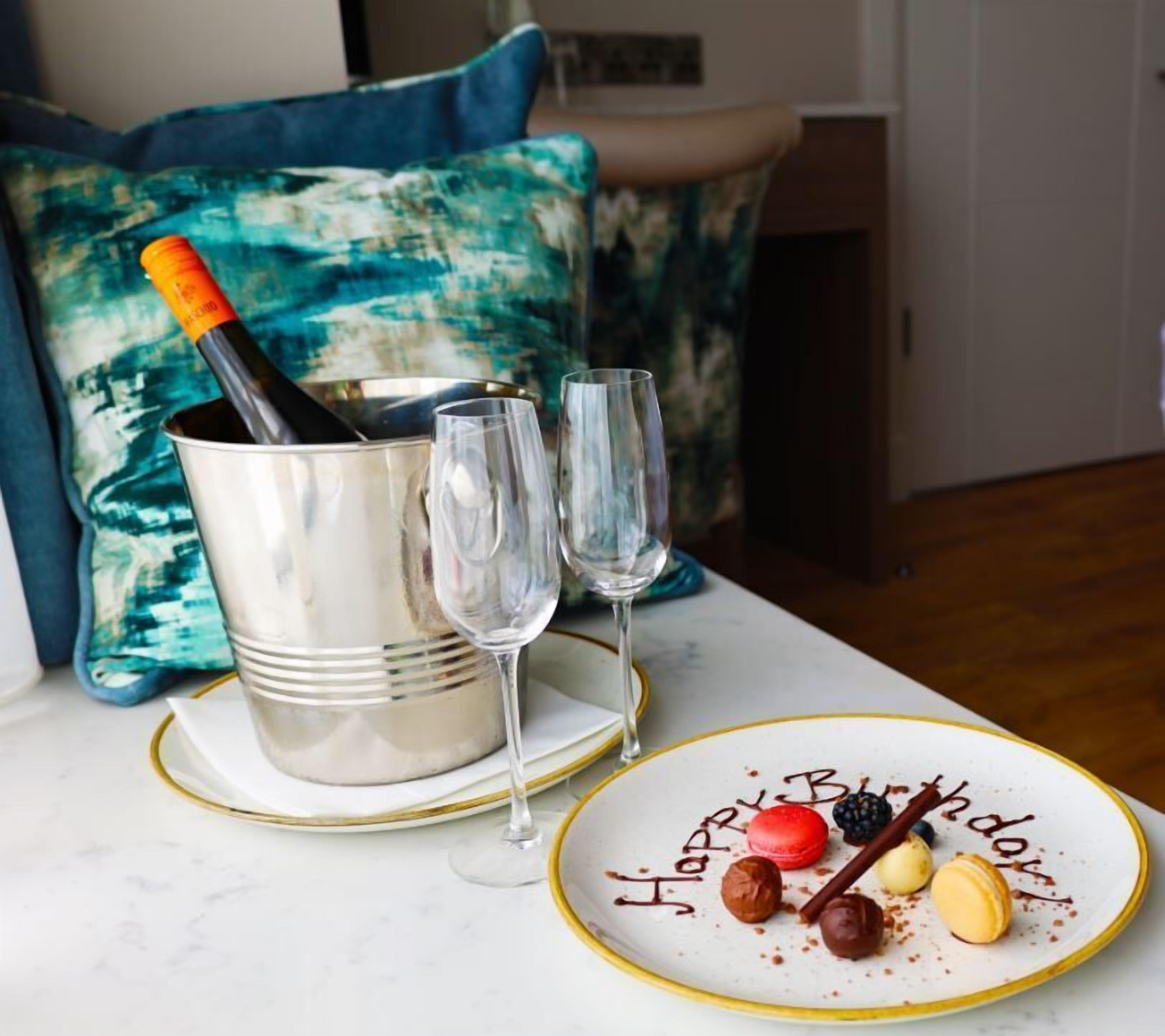 A table with a champagne bottle, two glasses, and a dessert plate with 'Happy Birthday' written on it.