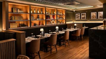 Een restaurant met houten boekenkasten, leren bankjes en een marmeren bar.