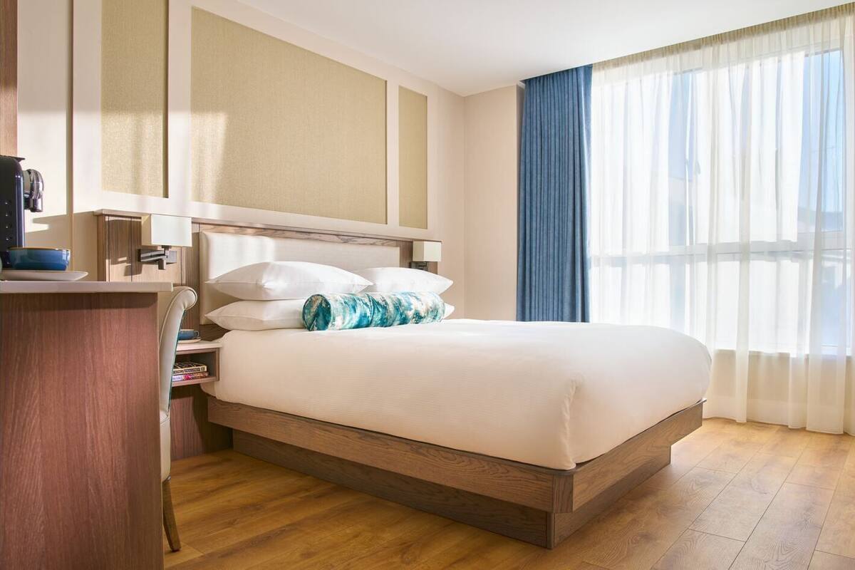 Une chambre d’hôtel avec un lit, un bureau, une lampe et une fenêtre avec des rideaux.