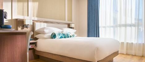 A hotel room with a bed, a desk, a lamp, and a window with curtains.