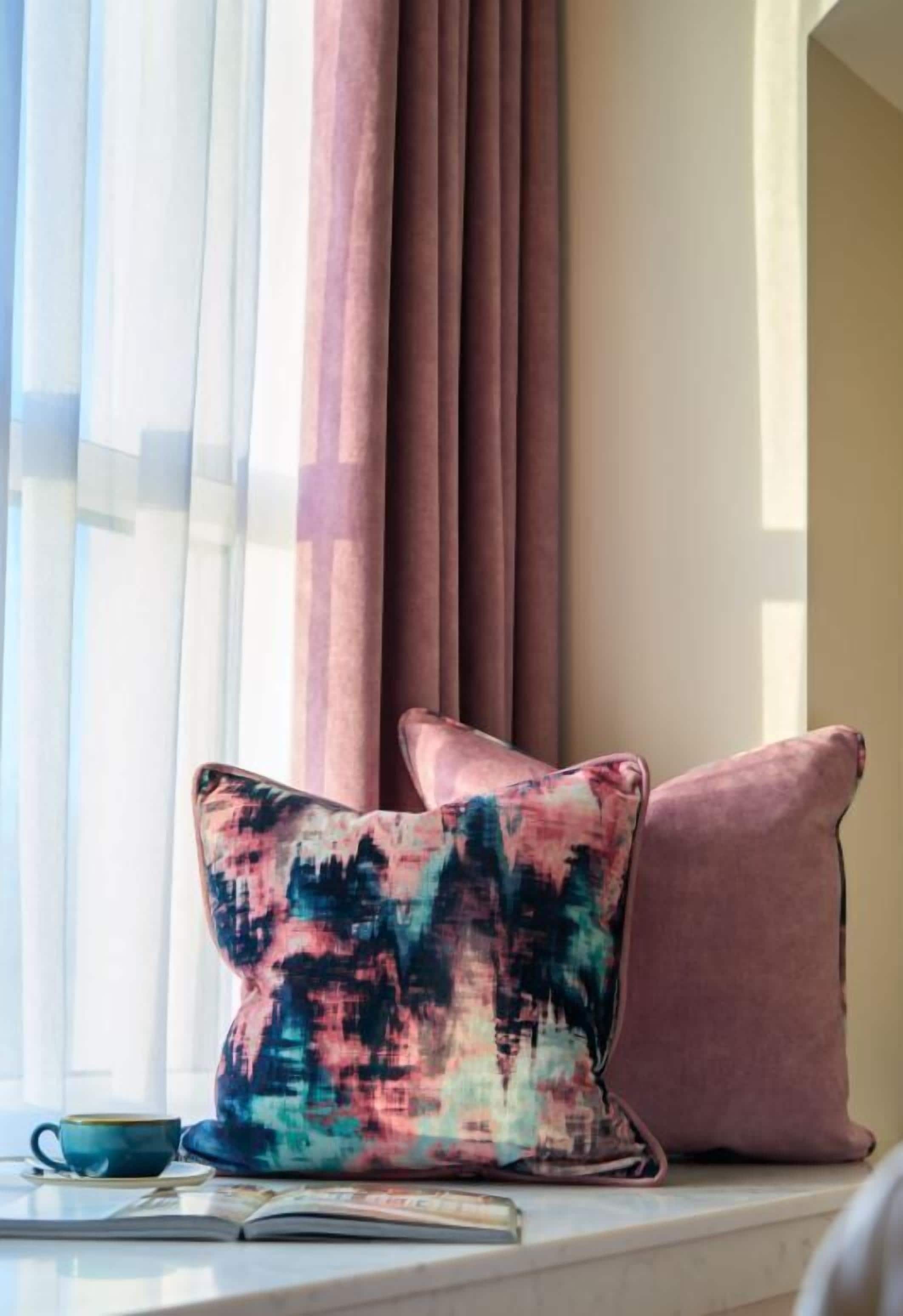 Asiento junto a la ventana con dos cojines, una taza y un libro.