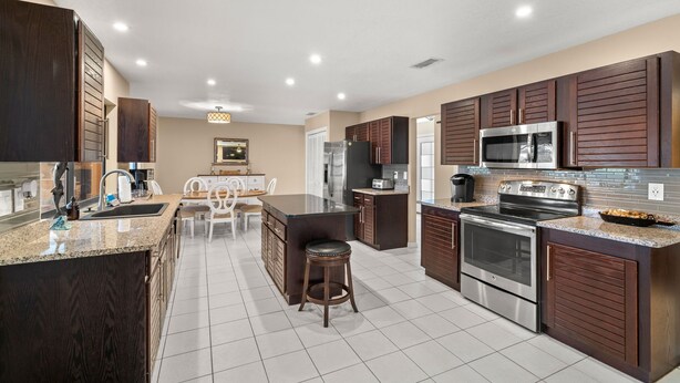 A modern kitchen with granite countertops, stainless steel appliances, and dark wood cabinetry. - Surfside Beach House | Pvt Pool, Grill, Office (Apollo Beach)