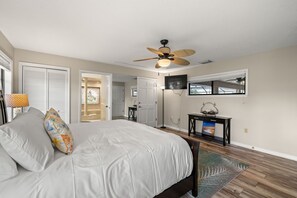 A bedroom with a bed, a ceiling fan, a TV, and a console table.