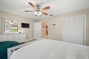 A bedroom with a bed, a ceiling fan, a dresser, a TV, and a closet. - Surfside Beach House | Pvt Pool, Grill, Office (Apollo Beach)