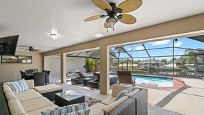 A spacious outdoor living area with a pool, comfortable seating, and a ceiling fan.