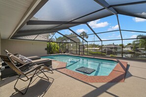 An indoor swimming pool with lounge chairs and a view of palm trees and houses.