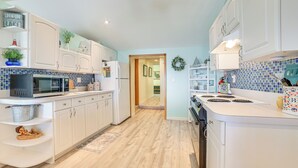 Cocina moderna con armarios blancos, microondas, estufa y lavaplatos. El suelo es de madera y el salpicadero está cubierto con azulejos azules.