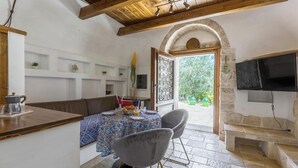 Un coin repas accueillant avec un plafond en bois, un banc en pierre et une table dressée avec une nappe bleue à motifs et des chaises.
