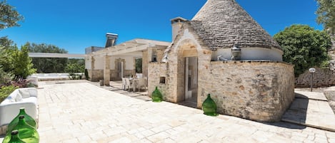 Un edificio de piedra con techo cónico, un patio empedrado y mesas al aire libre.