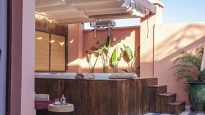 Un'area benessere con una panca in legno, un piccolo tavolino rotondo e una grande pianta in vaso.