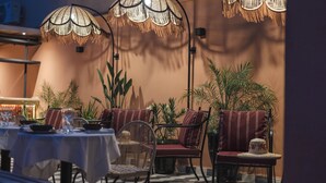 Un'area pranzo all'aperto con tavoli e sedie, circondata da piante in vaso e decorata con lampade sospese.