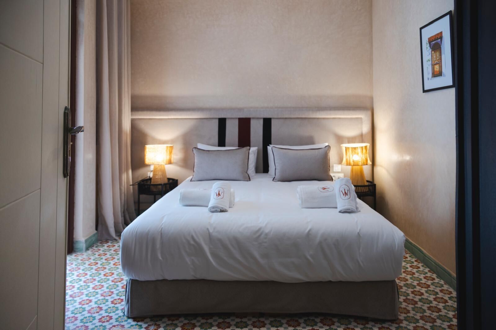 Une chambre d’hôtel avec un grand lit, deux tables de chevet avec des lampes et un sol à motifs.